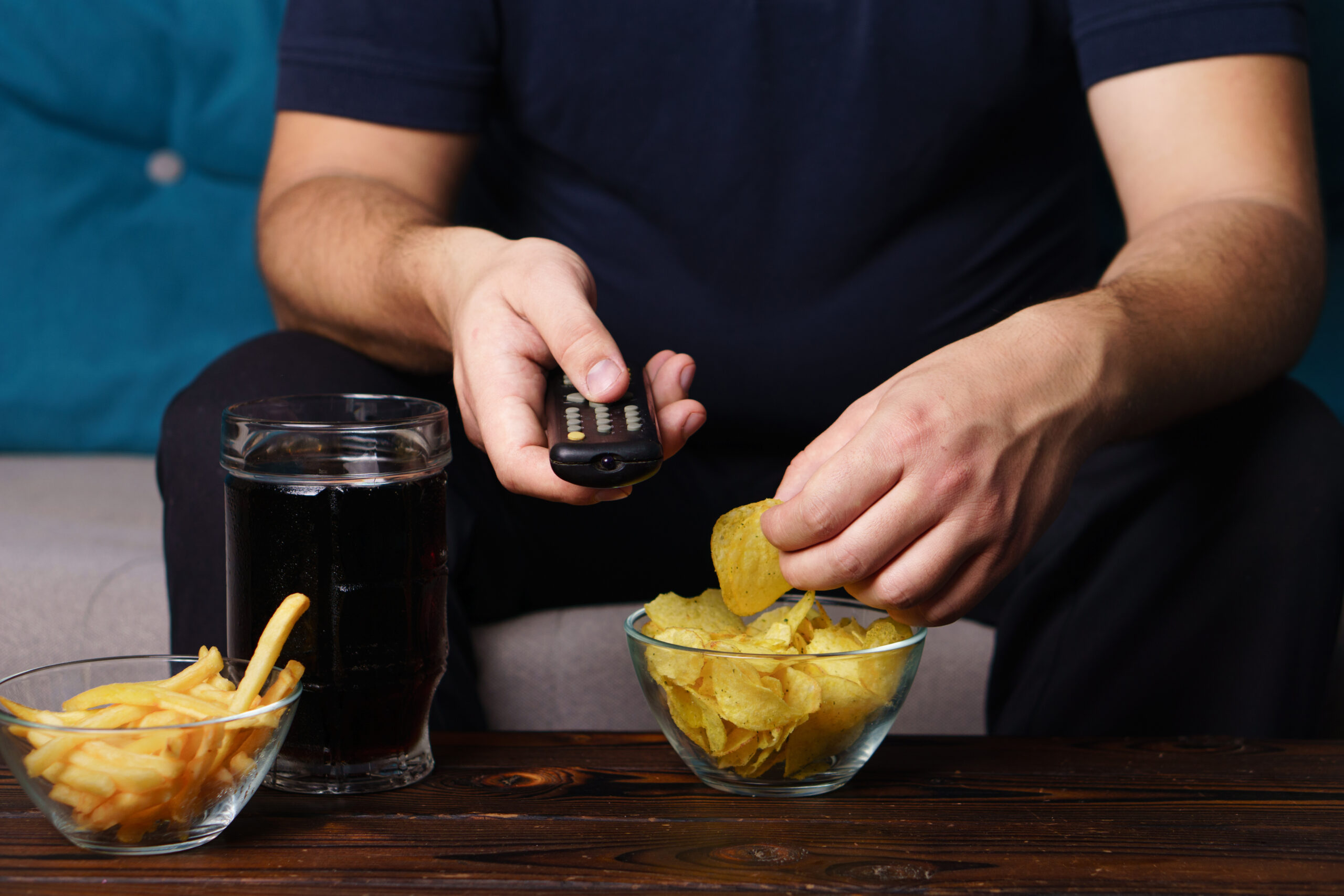 a man watching while eating chips and soda